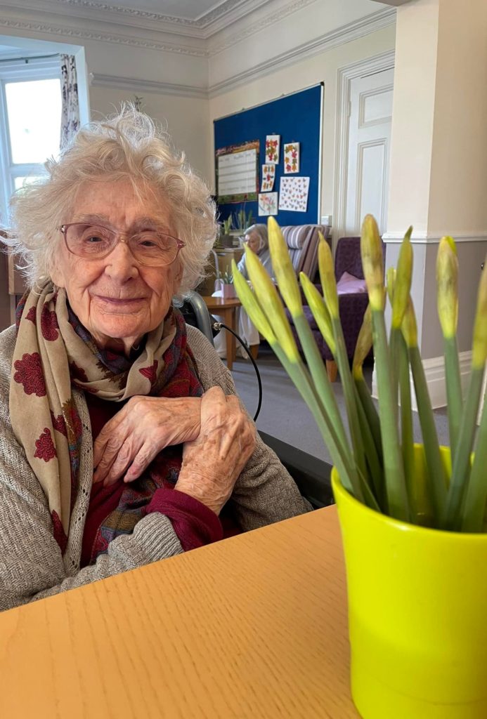 elderly woman smiling beside some flowers