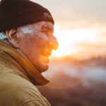 man in brown jacket and black hat in front of a sunset