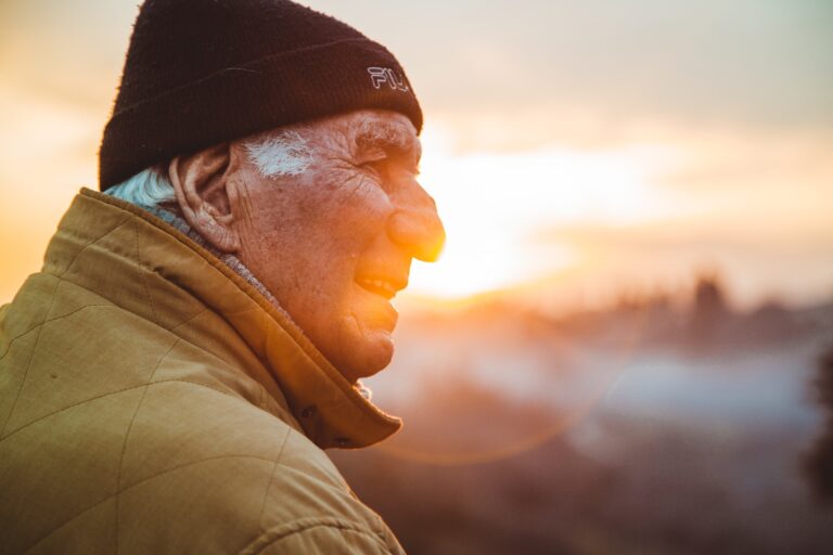 man in brown jacket and black hat in front of a sunset