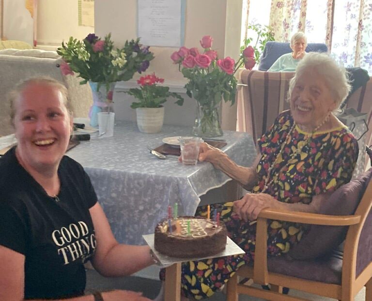 care home carer giving cake to elderly resident