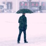 man walking in snow with umbrella