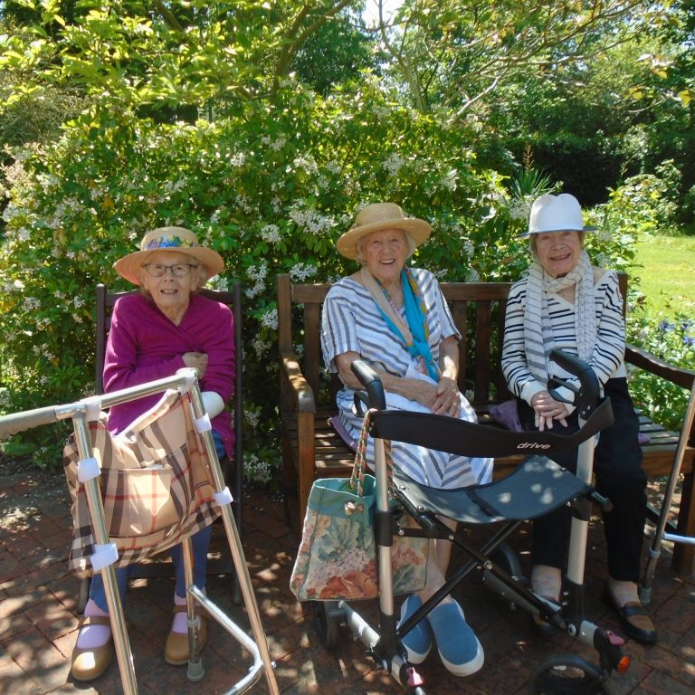 our care home residents sitting on a bench beside a green hedge