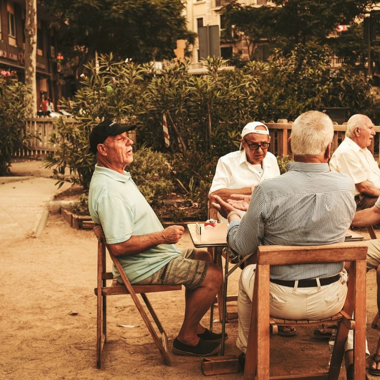four elderly men sitting around a table outside