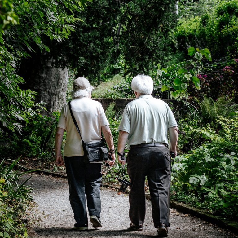 two elderly people walking through trees