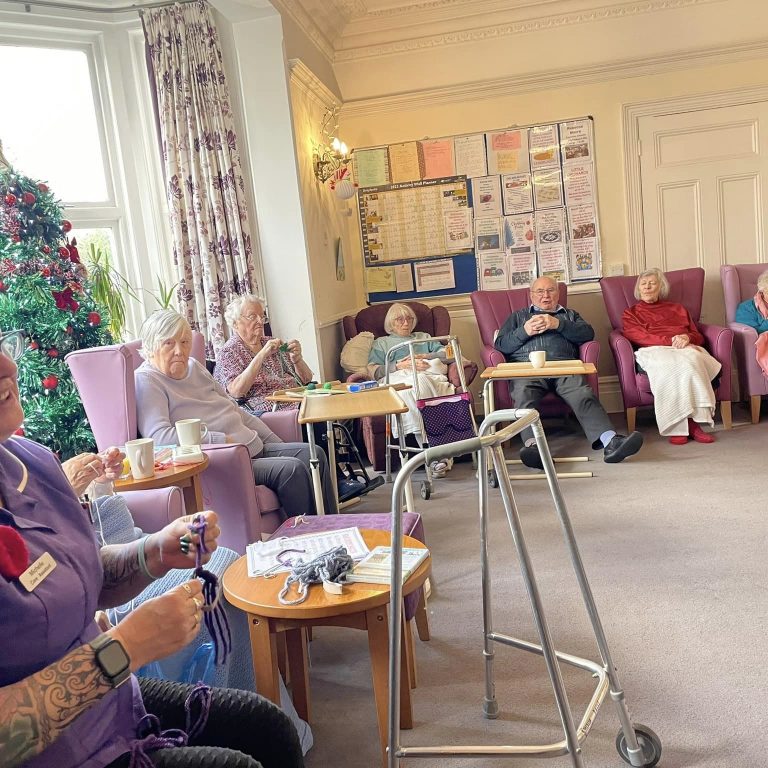 elderly people and carer knitting together
